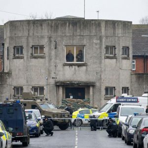 인질이 있는 요새화된 건물 안쪽으로, 창문과 문을 막고 방어 태세를 취한 무장 테러리스트들의 긴장된 대치 상황을 보여준다.